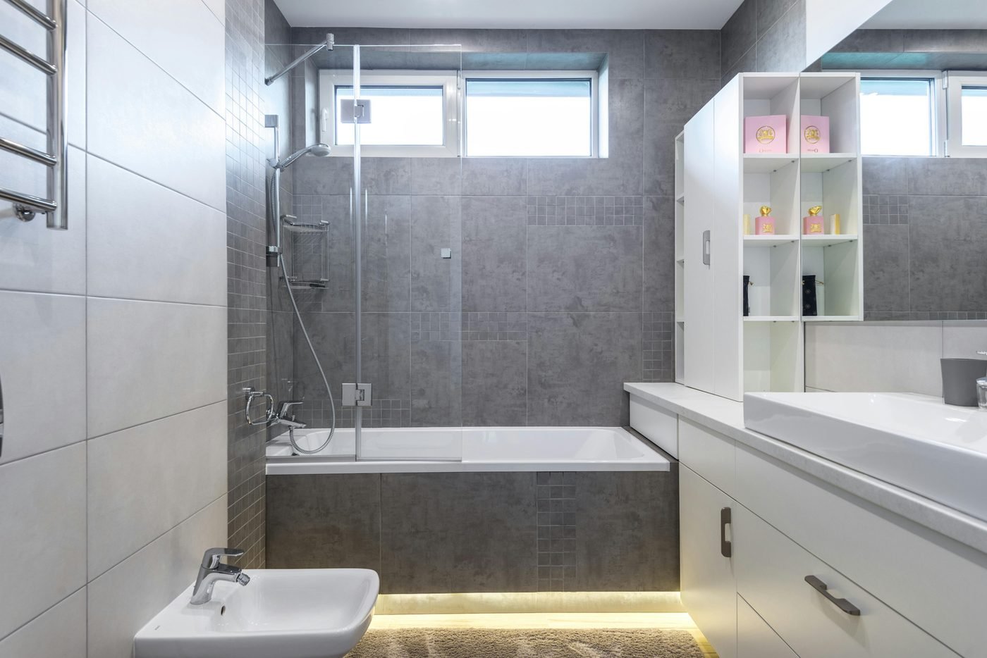 Bathroom with a glass-enclosed shower and tub, grey tile and white shelving