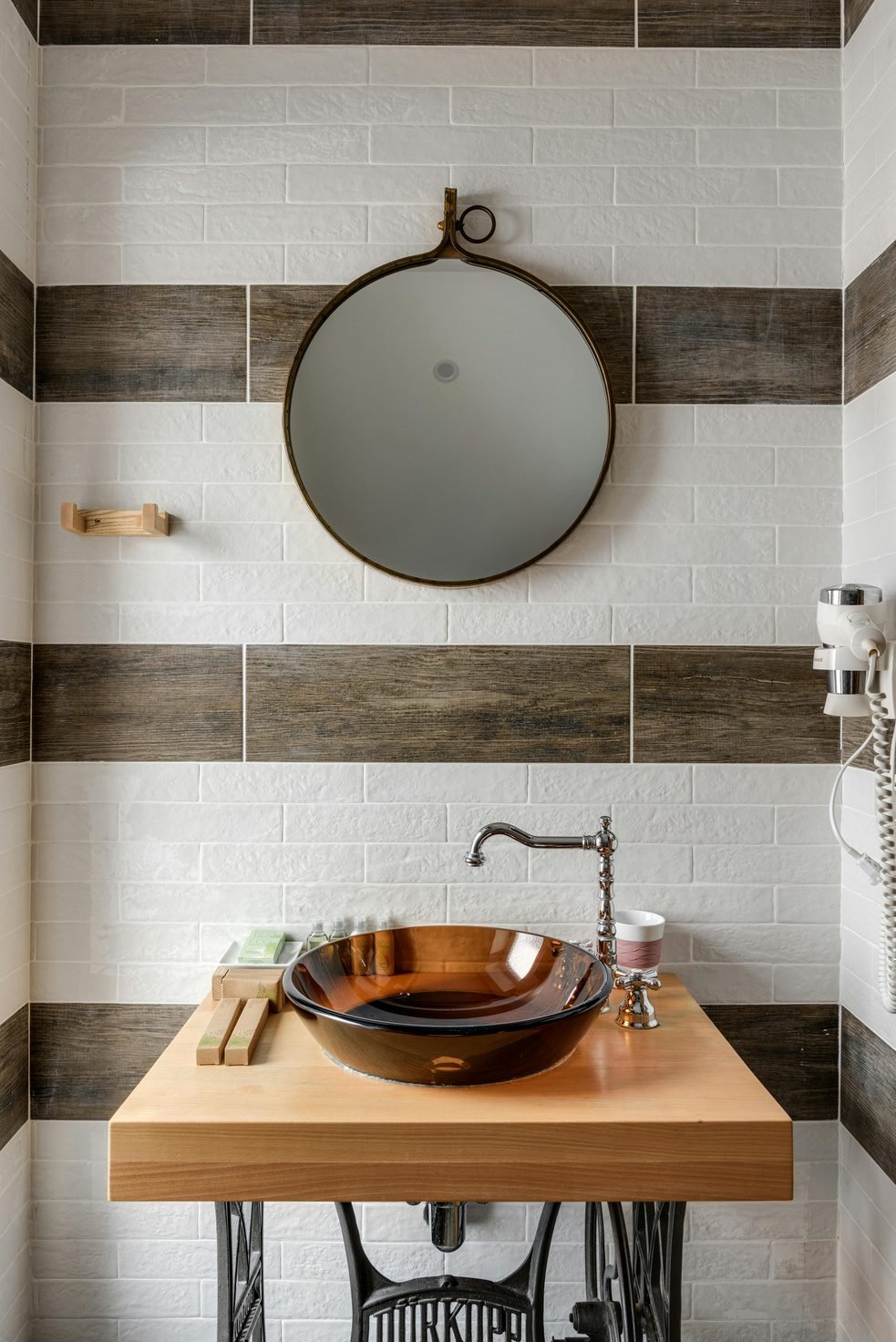 Wooden vanity with a copper vessel sink against striped white and wood-look tile