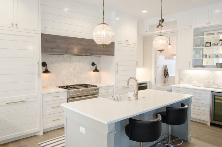 White kitchen with a stone hood, herringbone backsplash and crystal pendant lights
